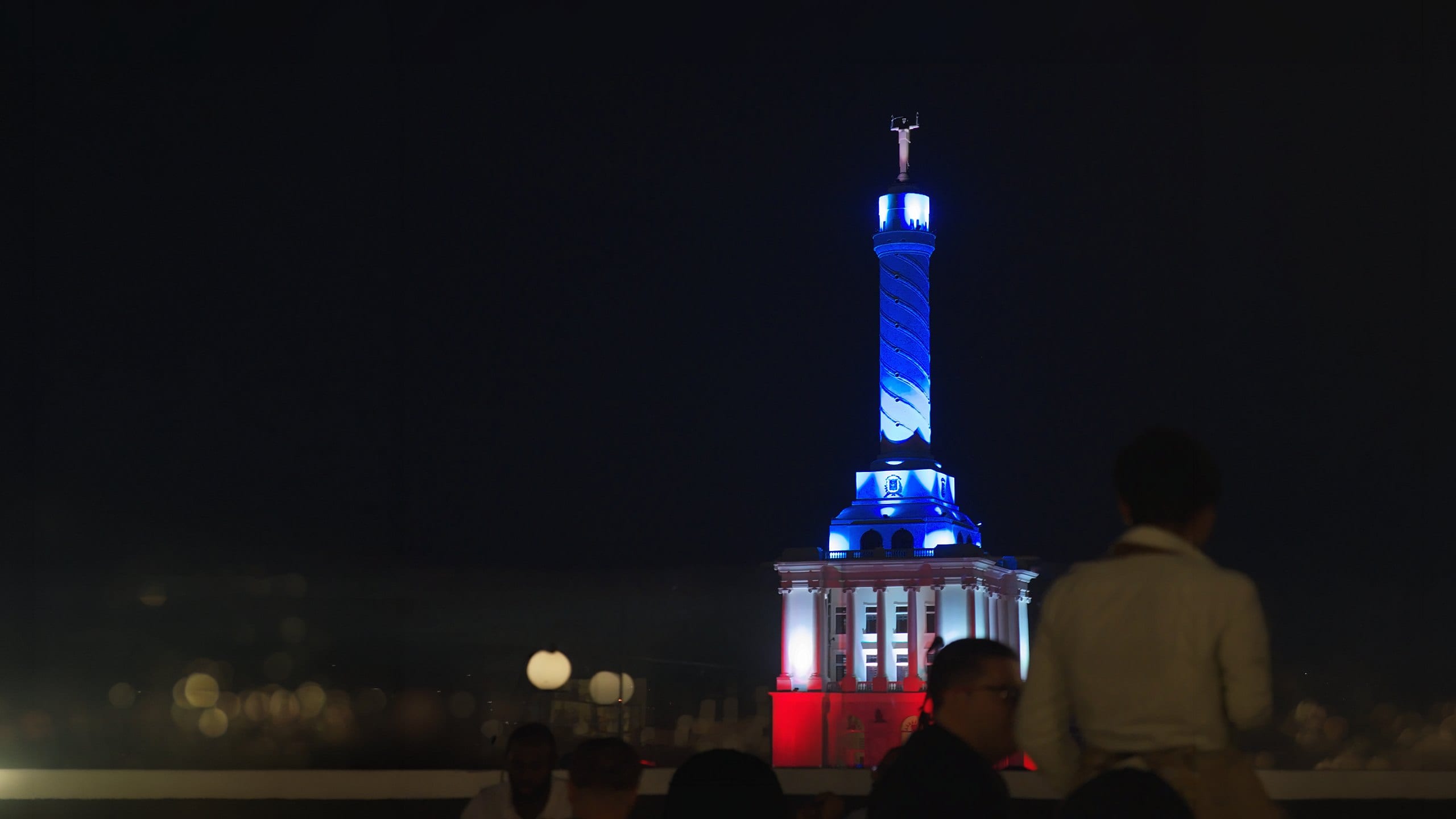El Monumento a los Héroes de la Restauración iluminado de noche, visto desde la terraza de El Diego